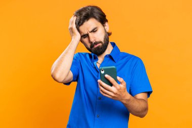 Adam cep telefonu akıllı telefon daktilosu kullanıyor. Ani piyango sonuçlarını kaybediyor. Kötü talih, kayıp. Orta Doğulu tişörtlü adam turuncu stüdyo arka planında tek başına kapalı bir yerde.