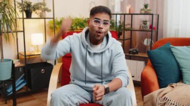 Mutlu Hintli adam bağırıyor, başarıyı kutluyor, kazanıyor, gol başarısı iyi haber piyango talihi zaferi, modern ev dairesinde TV şampiyonluğu izliyor. Oturma odasında oturan Arap adam.
