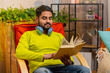 Hintli adam ilginç kitaplar okuyor, sayfaları çevirip gülümsüyor edebiyattan zevk alıyor, rahat koltukta dinleniyor. Huzurlu Hintli adamın portresi. Evde, sandalyede dinleniyor.