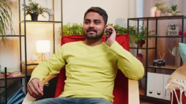 Telefon, iyi haber, dedikodu. Mutlu Hintli adam akıllı telefondan hoş sohbetler ediyor, modern ev odasındaki arkadaşlarıyla konuşmaktan keyif alıyor. Cep telefonundan hoşlanan adam konuşuyor