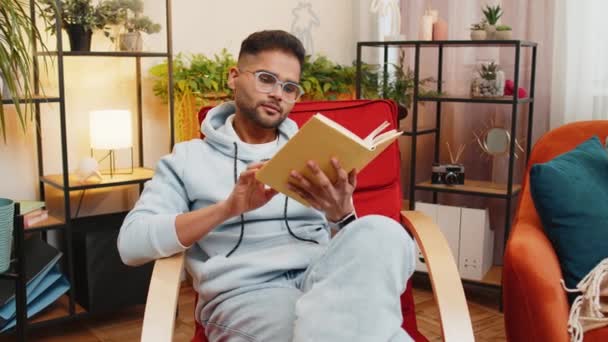 남자는 흥미로운 문학을 즐기는 페이지를 편안한 의자에 휴식을 의자에 아파트 — 비디오