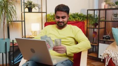 Planlama bütçesi. Zengin, mutlu Hintli adam para sayıyor dizüstü bilgisayar kullanıyor evde faturaları hesaplıyor. Arap adam kazancından memnun, planlı tatil için para biriktiriyor, hediyeler