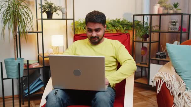 ラップトップコンピュータを使用して驚いたインドの若者は 突然の勝利に衝撃を受けたメールの良いニュースメッセージを受け取ります 宝くじジャックポット勝利 椅子の自宅のアパートでオンラインショッピングゲームを購入 — ストック動画