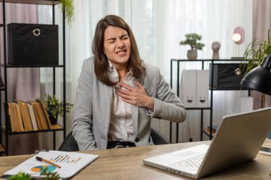 Dizüstü bilgisayar kullanan Kafkasyalı genç iş kadını, ofis masasında çalışırken kalp krizi geçirme riski nedeniyle göğsünde gerginlik yaşıyor. İş yerinde serbest çalışan bir kız..