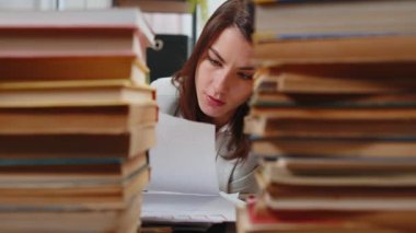 Yorgun Kafkasyalı iş kadını, ofis masasında çalışırken evrak raporlarına bakıyor. Yalnız başına stresli kız çaresizlik içinde kafaya dokunuyor. Masadaki kitap yığınlarıyla çevrili..