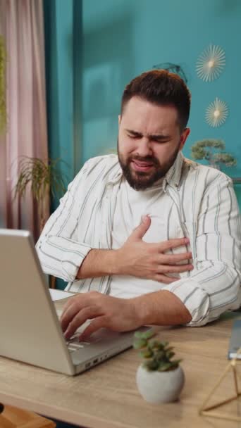 白人若いフリーランサーの男性は 病気を感じる脳卒中圧力症状の心臓痛発作のリスクを抱える緊張に苦しんでいます ひげ付き男は 自宅のオフィステーブルの職場に座っています バーティカル — ストック動画
