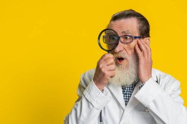 Araştırmacı bilimadamı kıdemli doktor kardiyolog elinde büyüteçle bakıyor, araştırıyor, analiz ediyor. Sarı arka planda eczacı dedesi. Kopyalama alanı