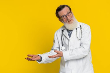 Kıdemli yaşlı doktor kardiyolog elini kaldırarak sorunların neden şüphe uyandırdığını soruyor. Eczacı eczanesi. Yaşlı büyükbaba sarı arka planda izole edilmiş.