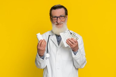 Kıdemli doktor kardiyolog, kabarcıklarda bir sürü hap olduğunu gösteriyor. İlaç, vitamin, antibiyotik tedavisi öneriyor. Sağlık hizmetleri. Eczacı dedesi sarı arka planda izole edilmiş.