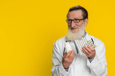 Kıdemli doktor kardiyolog, kabarcıklarda bir sürü hap olduğunu gösteriyor. İlaç, vitamin, antibiyotik tedavisi öneriyor. Sağlık hizmetleri. Eczacı dedesi sarı arka planda izole edilmiş.