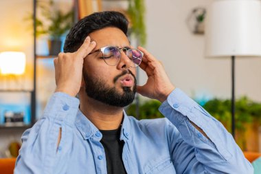 Hasta Hintli adam baş ağrısı problemini tedavi etmek için tapınakları ovuyor, tansiyon, migren, stres, acı, yüksek tansiyon. Evdeki koltukta oturan İspanyol adam.