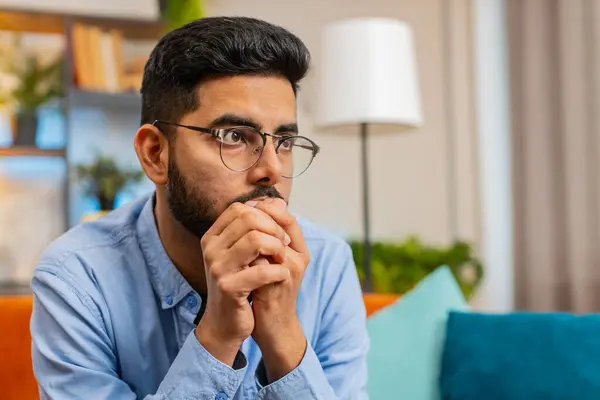 Serious tired Indian man sitting at home looks pensive nervous thinks over life concerns or unrequited love, suffers from unfair situation. Problem, break up, depressed feeling bad annoyed, burnout.