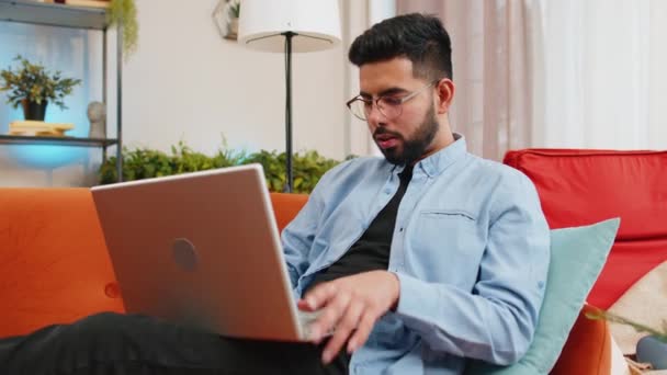 ハッピーインディアン男性は ラップトップを閉じるソファに座ってリラックスしてリビングルームで仕事を終えた後 若い男のフリーランサーは 自宅のソファーでオンラインリモートの仕事をしています Eラーニング ネットブックでの閲覧 — ストック動画
