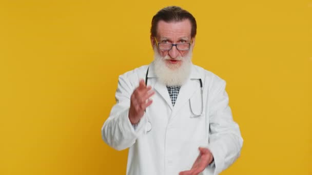 上級医師の心臓専門医は指を振り ノーと言い 危険な間違い 不承認サインを避けるためのアドバイスをし 喧嘩を嫌う 黄色の背景に薬局の祖父 — ストック動画