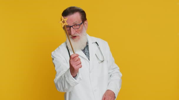 魔法使いの魔法使い 魔法の杖を作る魔法の杖を持つ高齢の医師の心臓病学者は 魔法の呪文 健康治療の助けをキャスティングして来ます 黄色の背景に薬局の祖父 — ストック動画