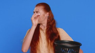 Kızıl saçlı çekici kadın kameraya gülümseyen bir şekilde tıbbi görüş lazer tedavisi ameliyatından sonra bardaklarını çöpe atıyor. Mavi stüdyo geçmişinde izole edilmiş güzel yetişkin bir kız.