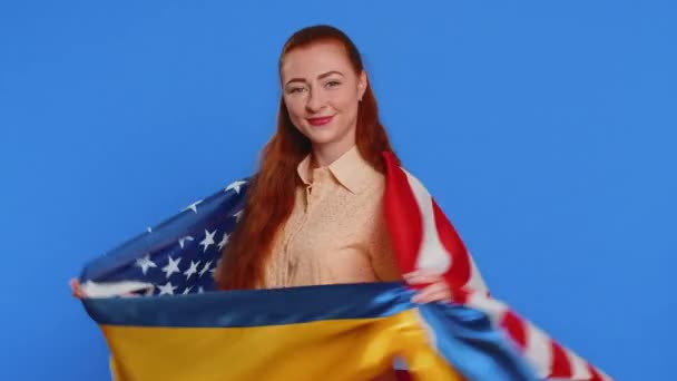 成年笑容满面的女人举着乌克兰和美国国旗 希望成功 战争胜利 支持帮助 被隔离在蓝色工作室背景下的女孩 — 图库视频影像