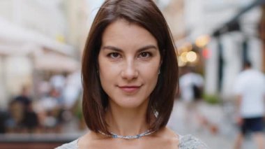 Mutlu genç kadının yakın plan portresi gülümseyen dost canlısı, mutlu gözler kameraya bakıp dinlenen rahatlama hayalleri kuran açık havada iyi haberler veriyor. Şehir sokağındaki güzel yetişkin kız.