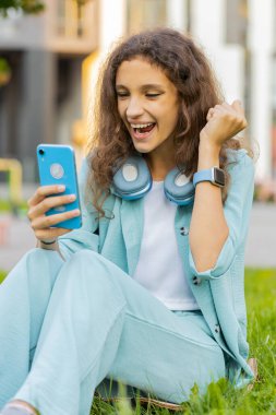 Ergenlik çağındaki çocuk cep telefonu kullanıyor. Kutlama yapıyor. İyi haberler alıyor, piyango ikramiyesi kazanıyor, internetten dağıtıyor. Şehir merkezindeki şehir parkında çimlerde oturan mutlu kız. Dikey