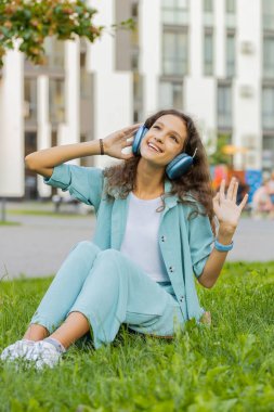 Telsiz kulaklıklı, neşeli, çocukluk çağındaki çocuk akıllı telefon dansında en sevilen disko rock n roll müziğini seçiyor. Şehir parkında çimlerde oturan bir kız. Dikey