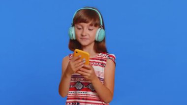 Genç liseli kız kulaklıkla müzik dinliyor, dans ediyor, eğleniyor, el kol hareketleri yapıyor. Beyaz çocuk mavi arka planda izole edilmiş akıllı telefon uygulaması kullanıyor.