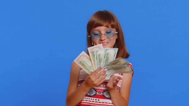 富人很高兴年轻可爱的女学生挥动钞票 像扇子一样的钞票 彩票中奖 丰厚的收入 工作室蓝色背景上的少女黑发女孩 — 图库视频影像