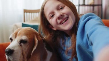 Şirin bir av köpeği ve oturma odasındaki kanepede selfie çeken neşeli bir kız çocuğu. Mutlu kız, prematüre evcil hayvan sever hafta sonu boyunca evde köpekle vakit geçiriyor.