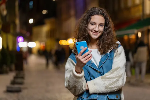 スマートフォンでテキストメッセージを入力して インターネットを閲覧し 仕事を終え カメラを見ている幸せな若い十代の少女 都市の通りを横断した女性 アウトドア タウン ロイヤリティフリーのストック画像