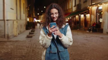 Gülümseyen mutlu genç kız akıllı telefon kullanıyor internete mesajlar yazıyor, işi bitiriyor, kameraya bakıyor. Gece şehir caddesinde silah omuza duran bir kadın. Şehir dışında..