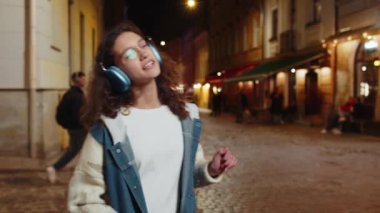 Kablosuz kulaklıklı mutlu, gevşemiş genç kız dışarıda akıllı telefonda dans ederek en sevilen disko rock n roll müziğini dinliyor. Gece şehir caddesinde yürüyen bir turist..