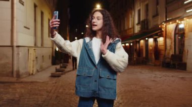 Mutlu ergen kız çocuk blogcu akıllı telefondan selfie çekiyor, sosyal medya vlog 'u için abonelerle çevrimiçi video görüşmesi yapıyor. Gece şehir caddesinde dikilen kadın