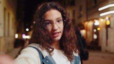 Genç kız blogcunun abonelerle internet üzerinden akıllı telefon iletişimi kurup sosyal medya vlog 'u için hikayeler kaydettiği POV görüşü. Geceleri şehir caddesinde mutlu genç.