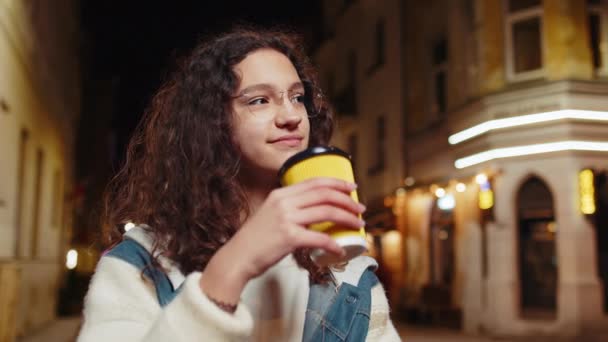 ハッピーブルネットの若い女性は コーヒーホットドリンクを楽しんで 遠く離れて考えている笑顔 リラックスして休憩 都会の街角のティーンエイジャーの少女は 屋外で夜にコーヒーを飲んでいる ライフスタイル — ストック動画