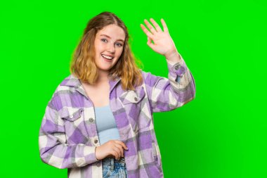 Kameraya gülümseyen beyaz bir kadın, el sallayarak selam veriyor ya da davetkar bir yüz ifadesiyle veda ediyor. Kızıl saçlı kız yeşil krom anahtar arka planında izole edilmiş.