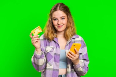 Kafkasyalı mutlu bir kadın kredi kartı ve akıllı telefon kullanıyor. Harcama parasını transfer ediyor, online alışveriş yapıyor, yemek siparişi veriyor. Kızıl saçlı kız yeşil krom anahtar arka planında izole edilmiş.