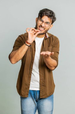 Biraz daha, lütfen bana ver. Hintli adam küçük bir jest yapıyor, kuşkucu bir gülümsemeyle minimum işaret veriyor, boyunu ölçüyor, yardım dileniyor. Arap adam gri stüdyo arka planında izole edilmiş.