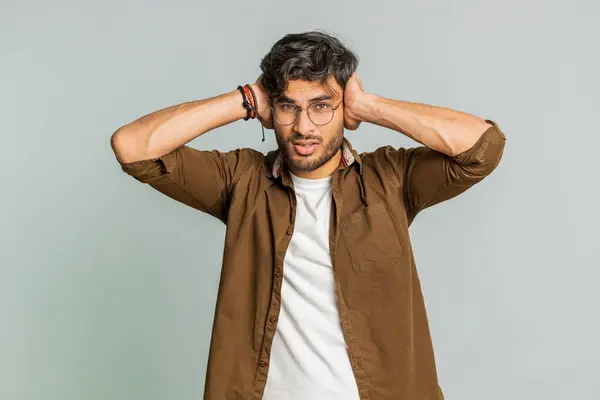 Dont want to hear and listen. Frustrated annoyed irritated Indian young man covering ears gesturing no, avoiding advice ignoring unpleasant noise loud voices. Arabian guy isolated on gray background