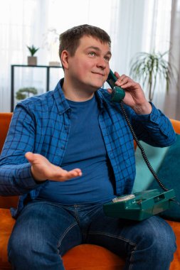 Evdeki rahat koltukta oturan arkadaşlarıyla telefon konuşması yapan genç beyaz adamın portresi. Mutlu, heyecanlı erkek. 90 'lardan kalma eski moda telefonlardan keyif alıyor.
