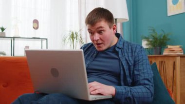 Laptop bilgisayar kullanan beyaz bir adam, iyi haber mesajı alıyor, evdeki kanepede piyango kazanma ikramiyesini kutlayan ani zaferi kutluyor. Yaşam Tarzları.