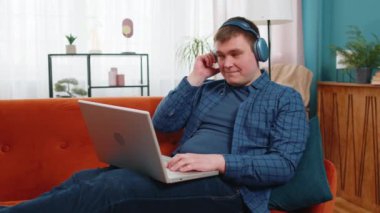 Happy, kablosuz kulaklıklı, aşırı neşeli Kafkasyalı, serbest çalışan, evinde oturmuş, dizüstü bilgisayar ağı üzerinde çalışırken disko müziği dinleyen genç adam. Erkekler hafta sonu aktiviteleri