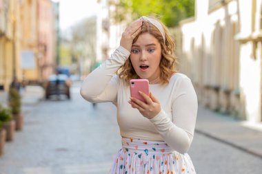 Akıllı telefon kutlaması yapan mutlu, genç, kızıl saçlı bir kız. İyi haberler, piyango zaferi, açık havada açık havada açık artırma. Şehir caddesinde duran gülümseyen kadın turist. Yaşam Tarzları.