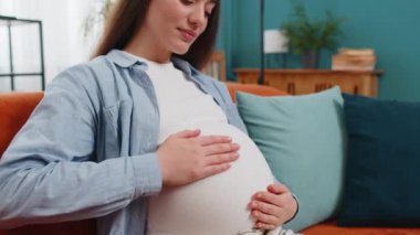 Evdeki rahat koltukta oturan, göbeğini okşayan, rüya gören, mutlu, hamile bir kadın. Hamilelik sırasında gülümseyen, beyaz, müstakbel kadın anne bebek bekliyor..