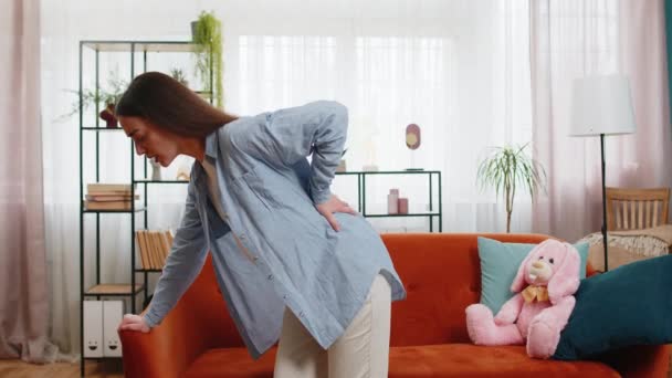 自宅のリビングルームでソファーのソファーに座って腰痛に苦しんでいる若い妊娠中の女性 将来の親 ソファに 触れる 大きな アパート — ストック動画