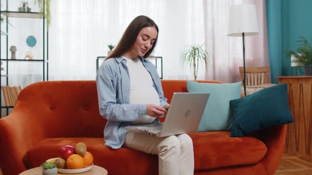 快乐的孕妇微笑着数钱在笔记本电脑上按键盘键 积极漂亮的白种人孕妇坐在沙发上 在家里网上购物 舒适和方便 — 图库视频影像