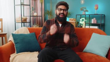 Mutlu Hintli adam bağırıyor, başarıyı kutluyor, kazanıyor, gol başarısı iyi haber piyango talihi zaferi, modern ev dairesinde TV şampiyonluğu izliyor. Oturma odasında oturan Arap adam.