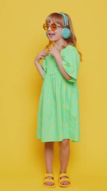 Kulaklıkla müzik dinleyen liseli kız ve dans eden disko partisi etrafta eğlenerek el kol hareketleri yapıyor. Sarı arka planda güneş gözlüklü beyaz çocuk. Dikey