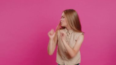 Neşeli, neşeli, genç bir kadın dans ederek ve ritim tutarak eğleniyor, ellerini ovuşturuyor, dublaj dansı kazanan jestler yapıyor. Mutlu kız pembe stüdyo arka planında tek başına. Yaşam Tarzları