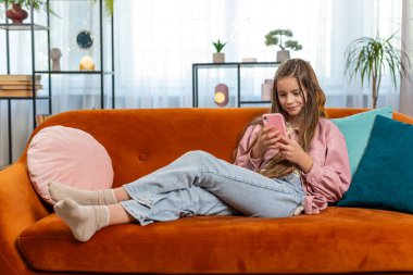 Akıllı telefon sosyal medya uygulamaları üzerinden rahatlama filmi izlerken mesajlarını paylaşan genç bir kız. Beyaz kız çocuk cep telefonu kullanıyor. Oturma odasındaki koltukta oturuyor.