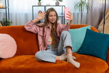 Mutlu genç kız blogcu akıllı telefondan selfie çekiyor sosyal medya abonelikleriyle internetten video görüşmesi yapıyor. Genç bir kız çocuk, evdeki kanepede video kaydediyor..