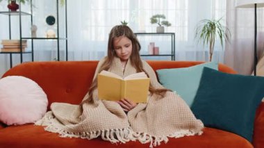 Genç beyaz çocuk battaniyeye sarılıp rahatlıyor ilginç kitaplar okuyor sayfalarca gülümsüyor edebiyattan keyif alıyor rahat bir kanepede dinleniyor. Evdeki oturma odasındaki kanepede oturan mutlu kız..
